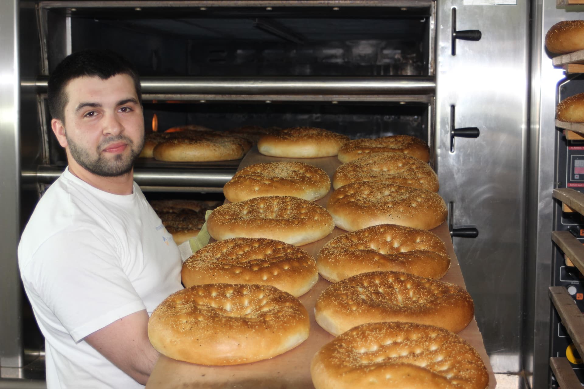 Bäcker der HAK Bäckerei mit einem Blech frisch gebackener Fladenbrote vor dem Ofen