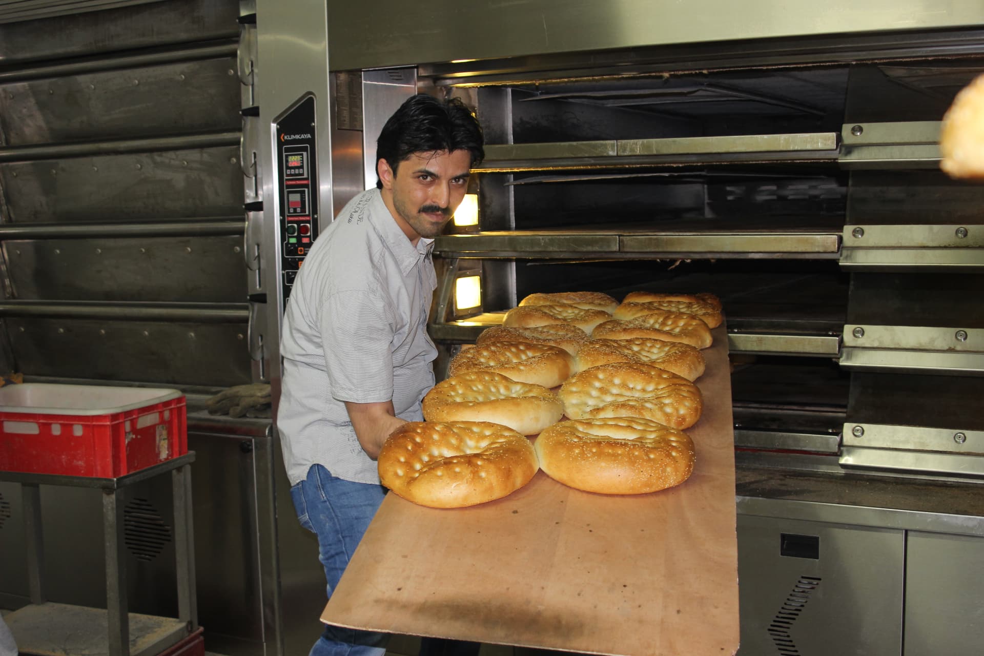 Bäcker der HAK Bäckerei mit einem Blech frisch gebackener Fladenbrote am Ofen